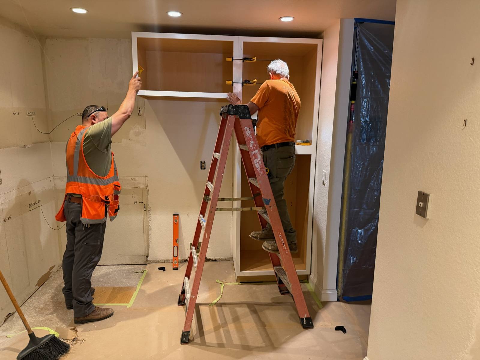 Elusive Construction crew installing kitchen cabinets over floor protection with dust containment in place