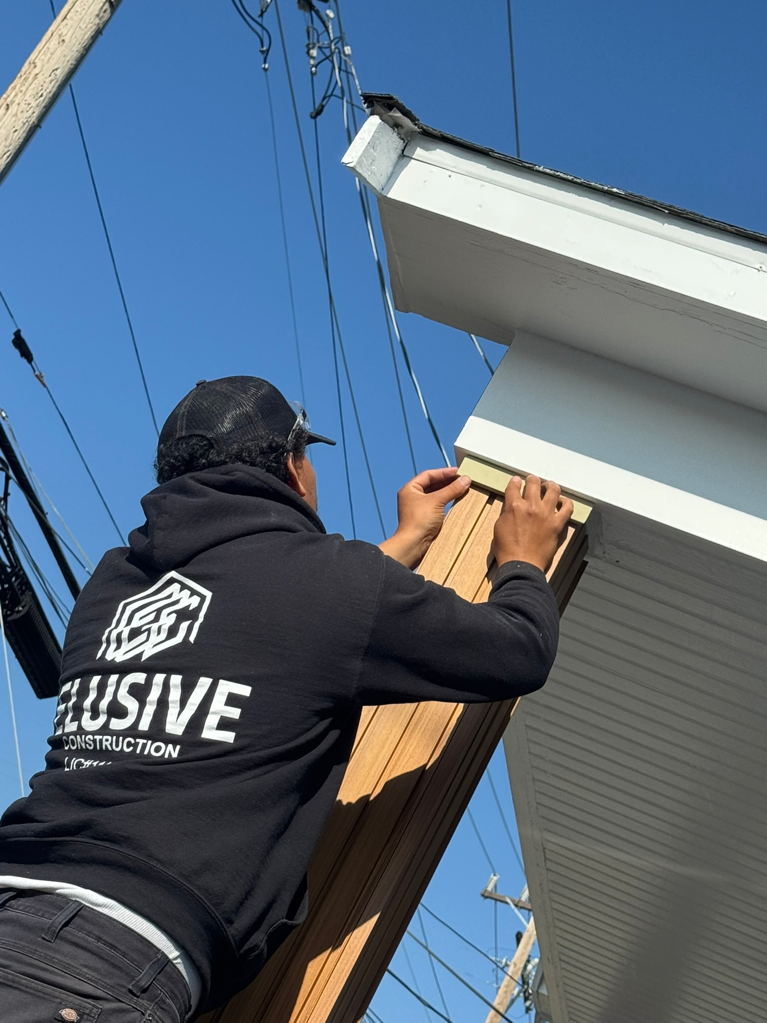 Elusive Construction crew member on a ladder fitting fascia trim on a San Jose home