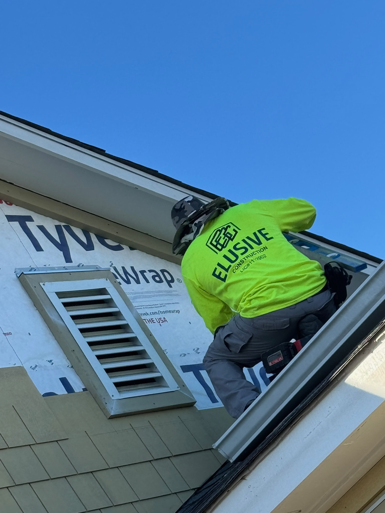 Elusive Construction crew member in a branded shirt running weather barrier at the roofline of a San Jose home
