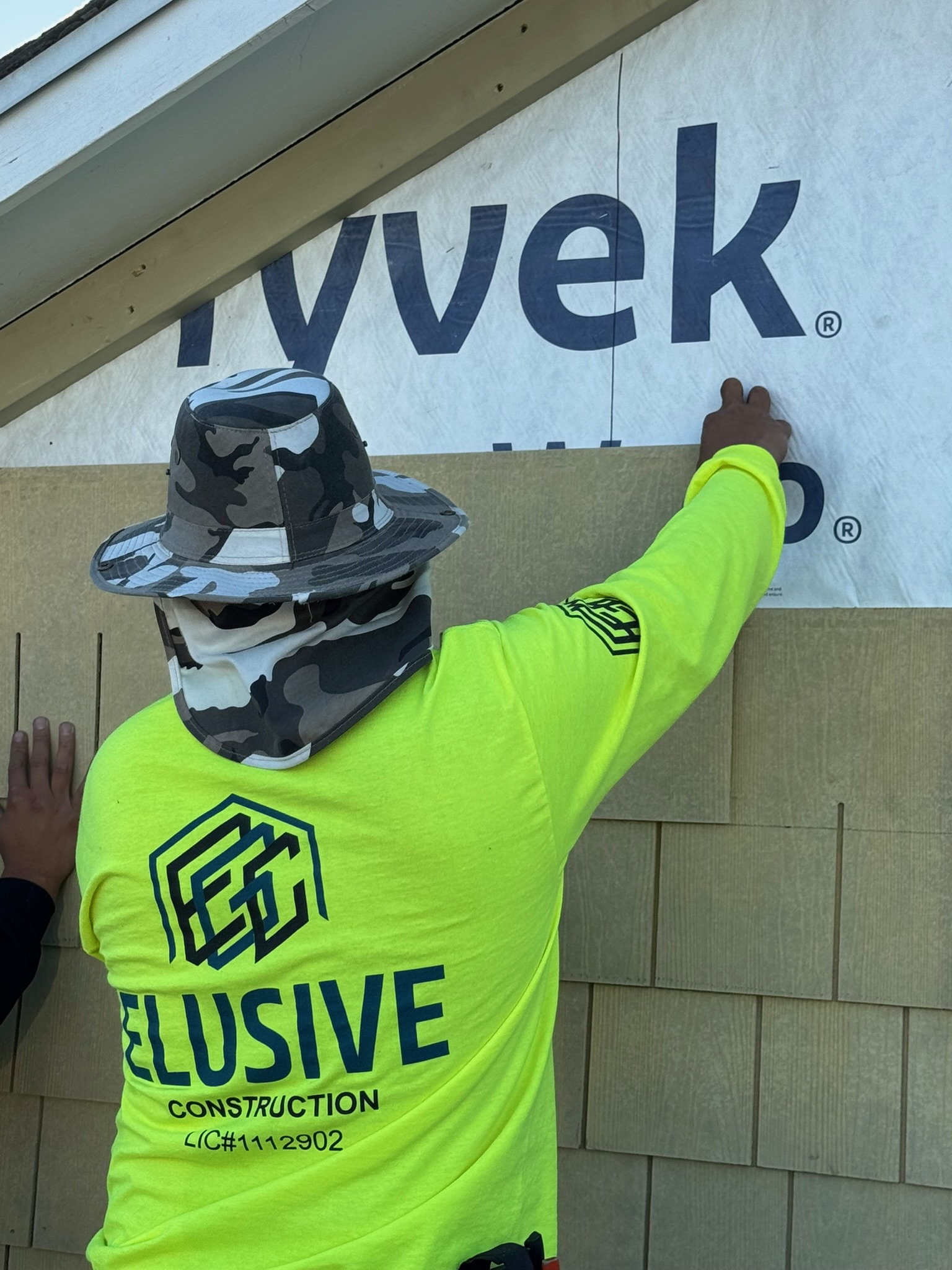 Elusive Construction crew member in branded hi-vis installing Tyvek weather barrier on a San Jose home