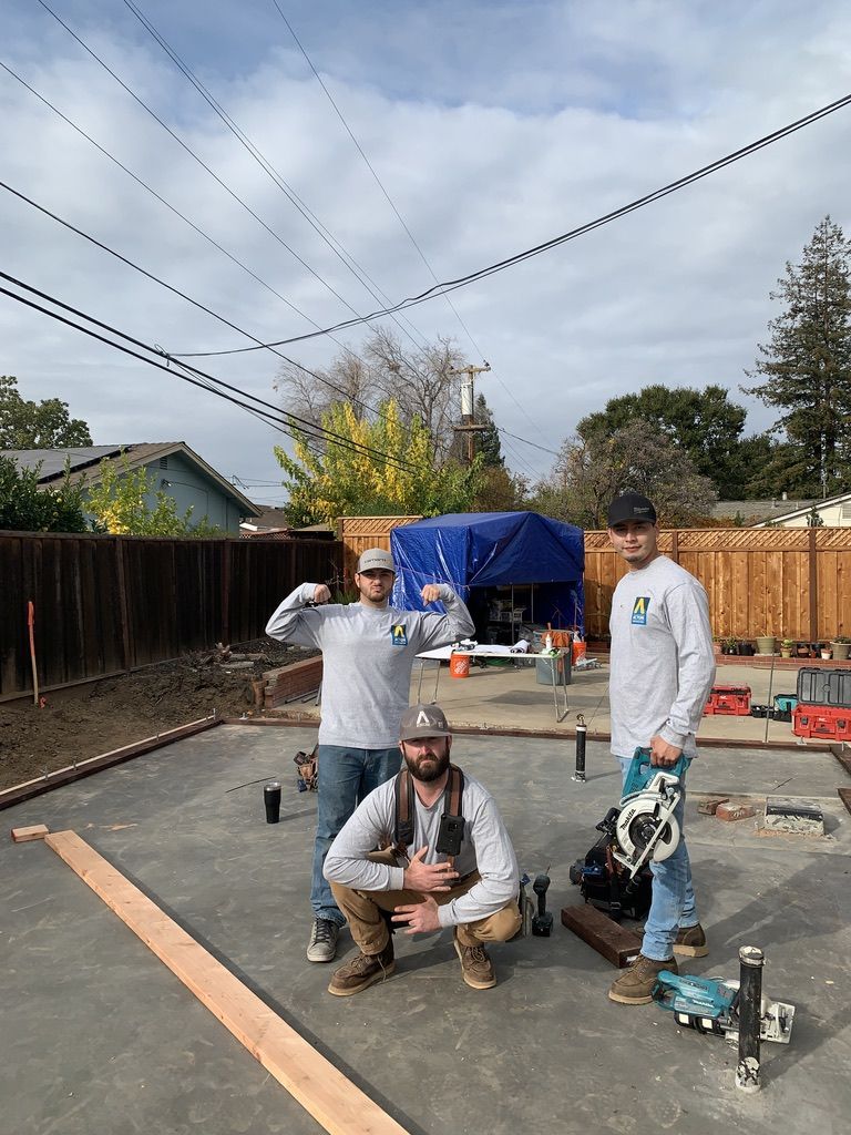 Three framers on a finished slab with plumbing stub-ups, tools and a mud sill laid out ready for framing