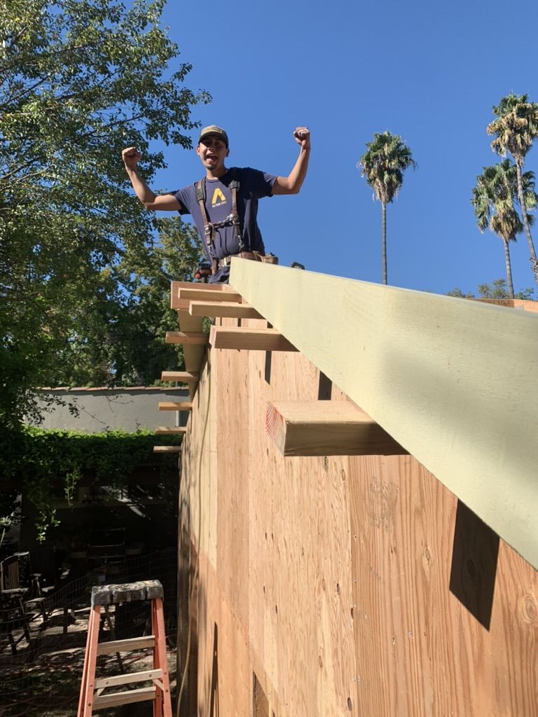 A framer standing on top of a newly framed and sheathed wall with a beam set, arms raised