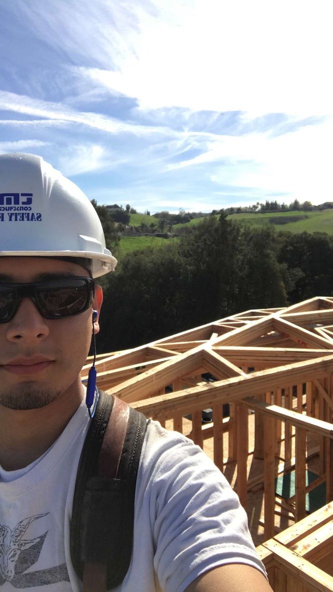 On a completed roof truss structure wearing a safety hard hat, open hills behind