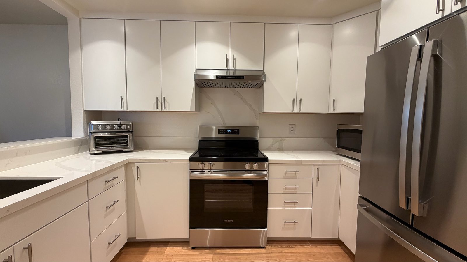 Completed kitchen refresh in San Jose with white flat-panel cabinets, light counters, a full-height slab behind the range and stainless appliances