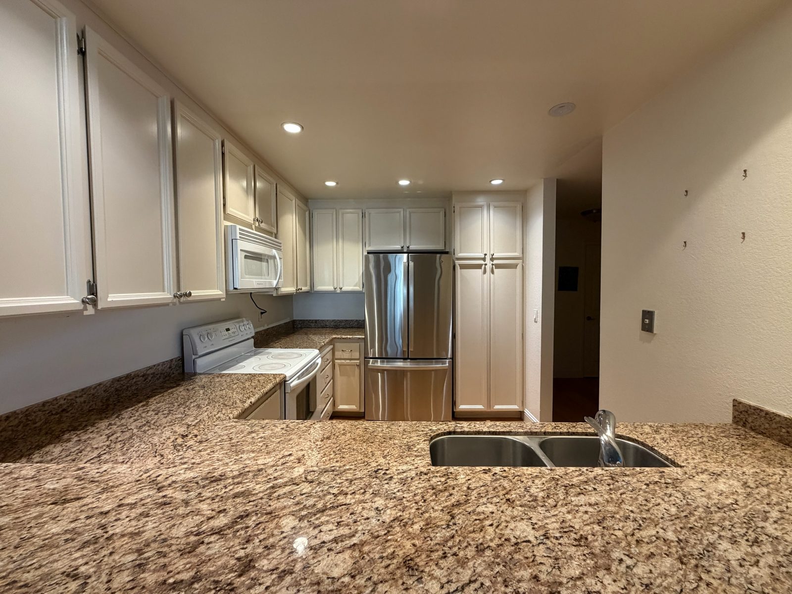 Kitchen before the refresh, seen from the peninsula: white raised-panel cabinets, speckled counters and white appliances