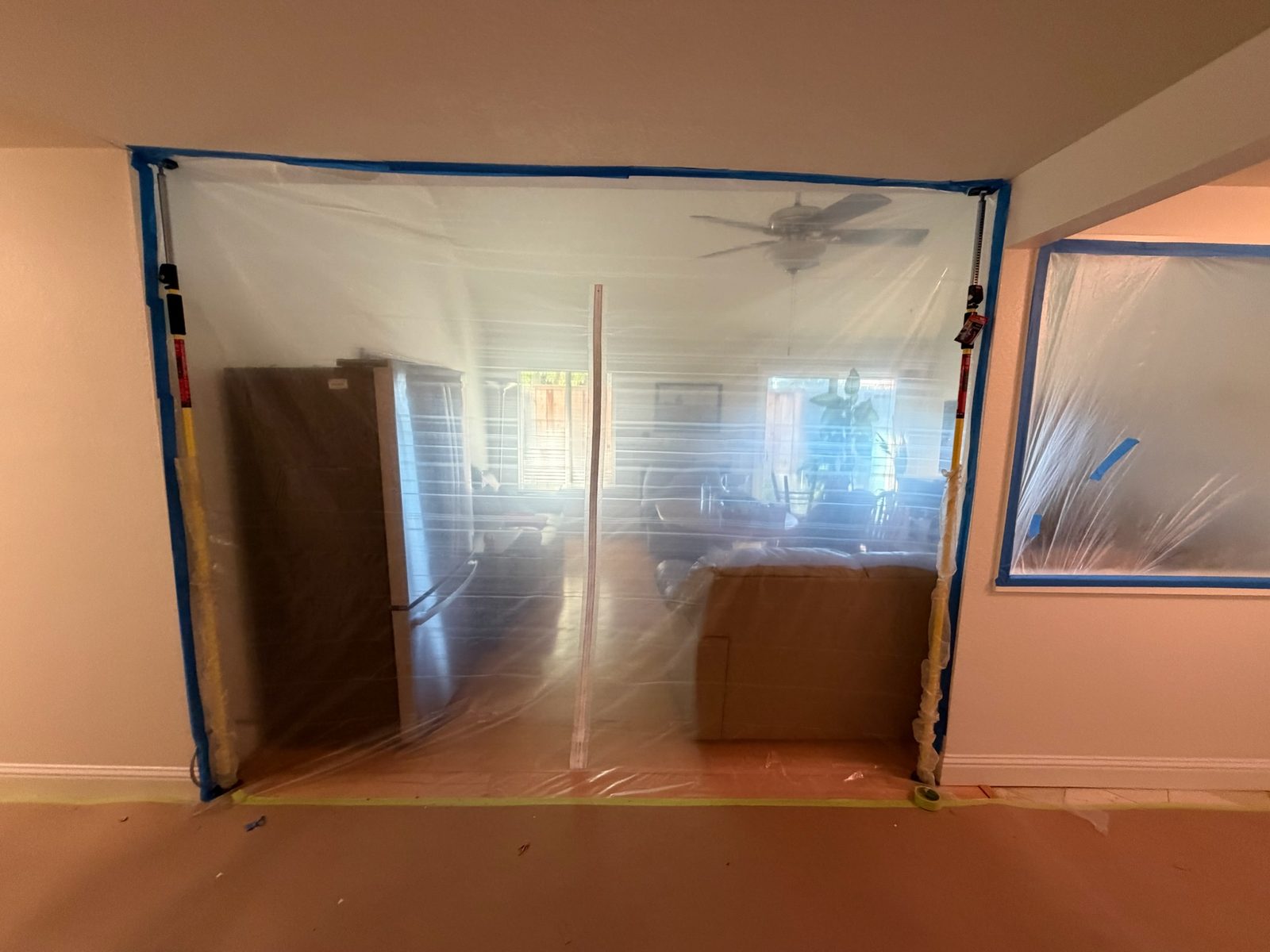 Sealed plastic dust barrier across the kitchen pass-through, with the refrigerator relocated to the living-room side