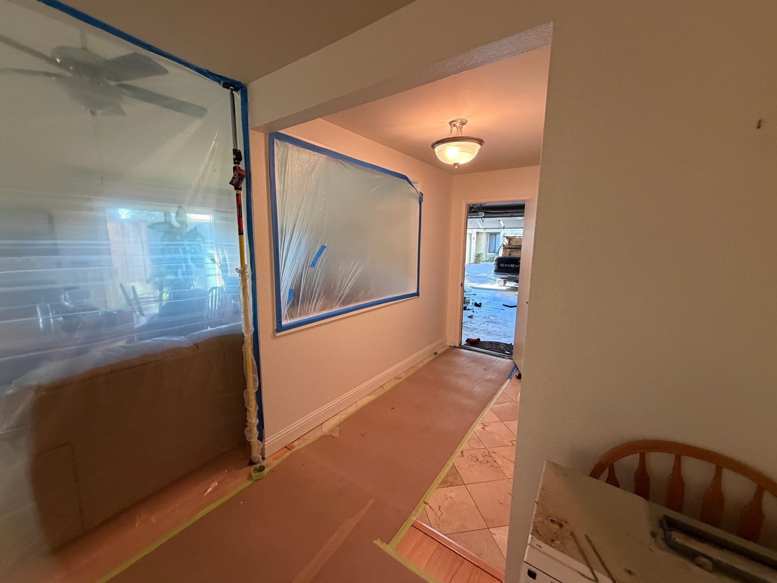 Protective paper taped over the floor from the kitchen to the front door, with the pass-through window sealed in plastic