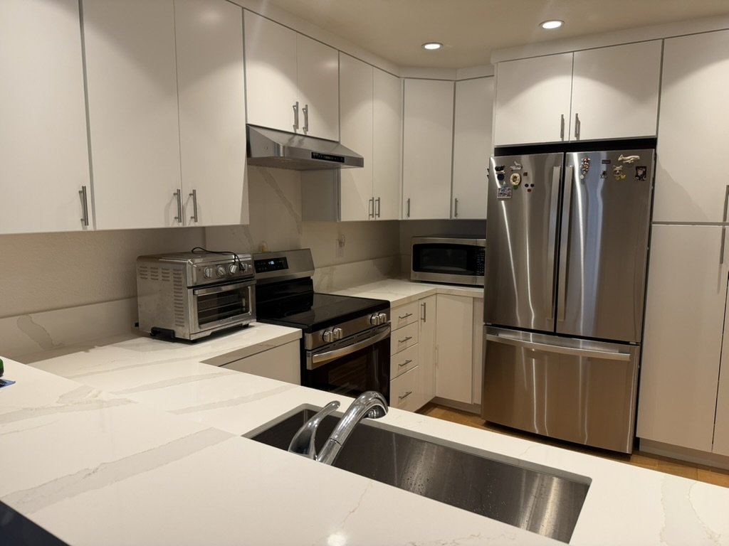 Kitchen in daily use after the refresh, range wall with full-height slab backsplash and stainless appliances